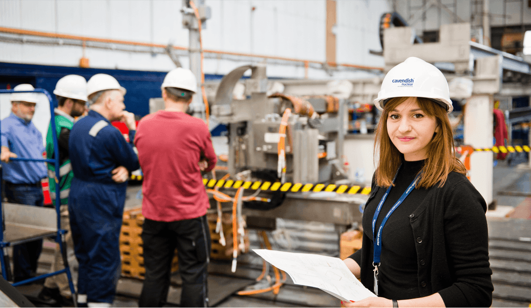 A woman wearing a hard hat is holding a piece of paper, indicating her involvement in a construction or engineering project.