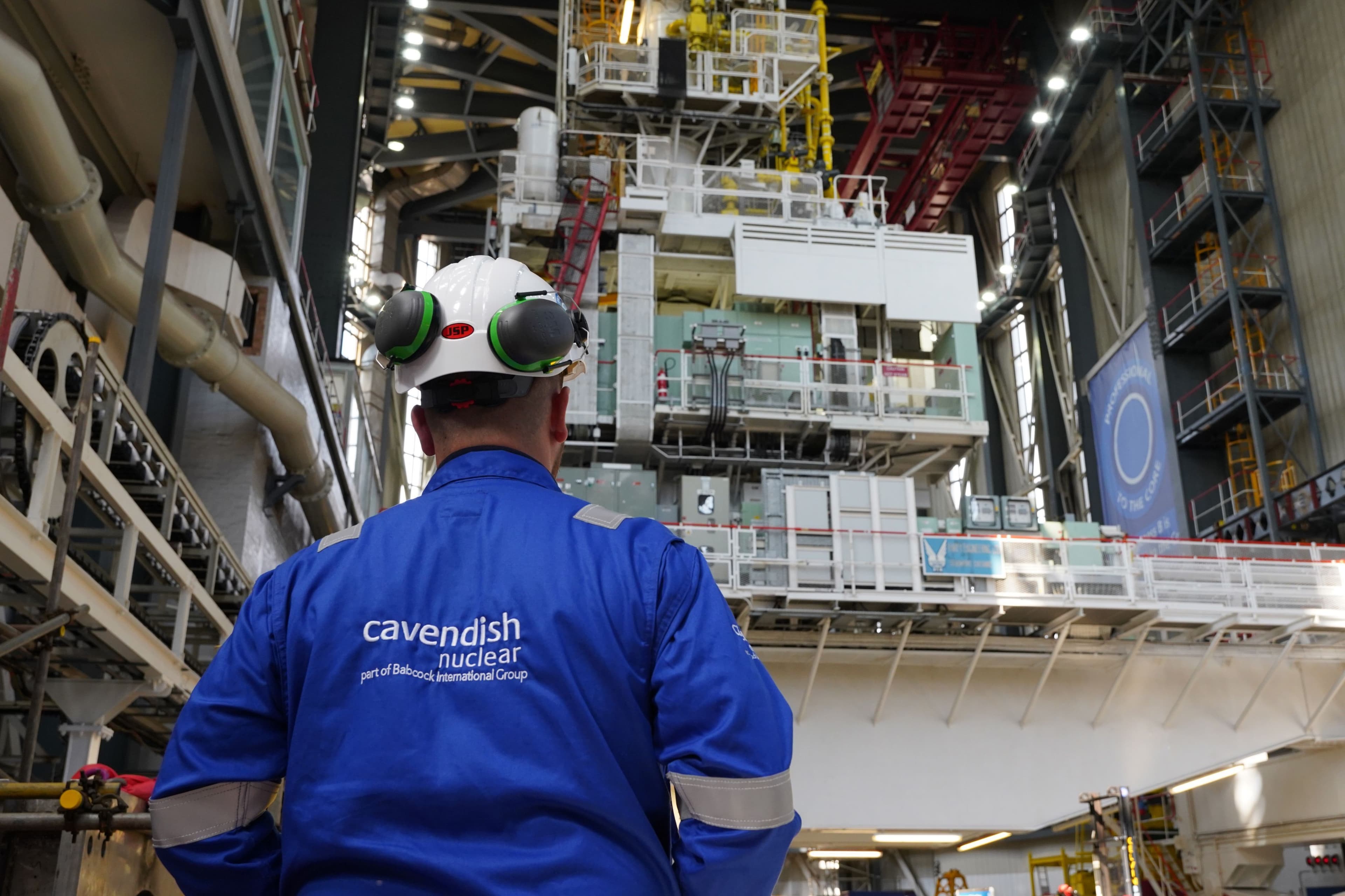 Worker in a “Cavendish Nuclear” jacket and hard hat looking into an industrial plant area